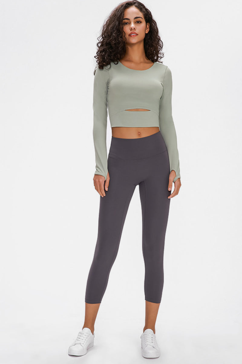 Woman wearing a long-sleeved, cropped workout top in green, fitted with a support strap, for high-impact activewear.
