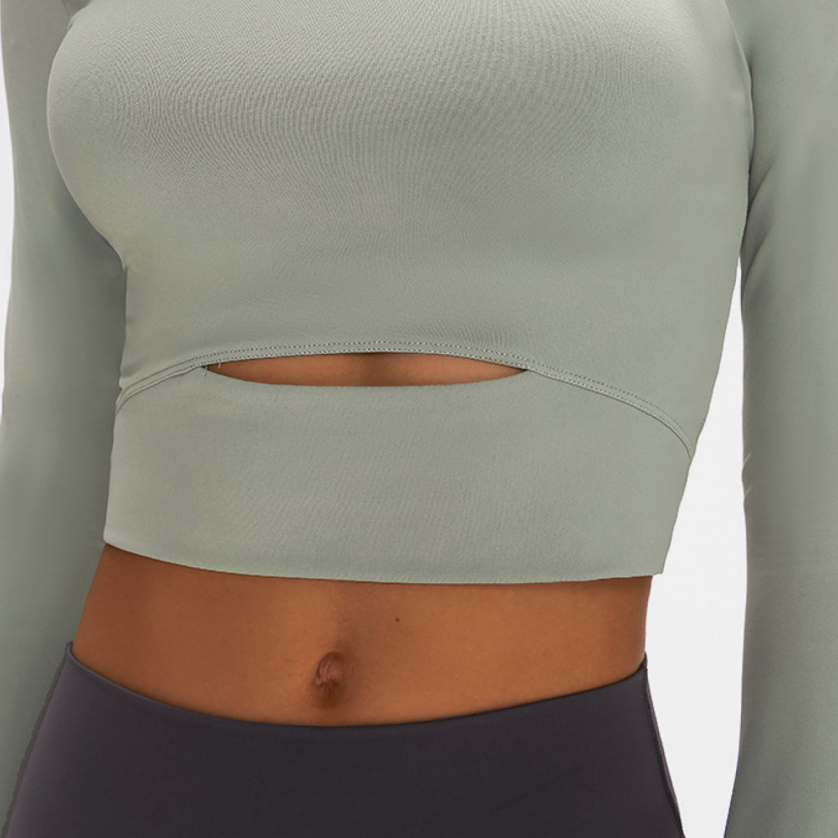 Woman wearing a long-sleeved, cropped workout top in green, fitted with a support strap, for high-impact activewear.