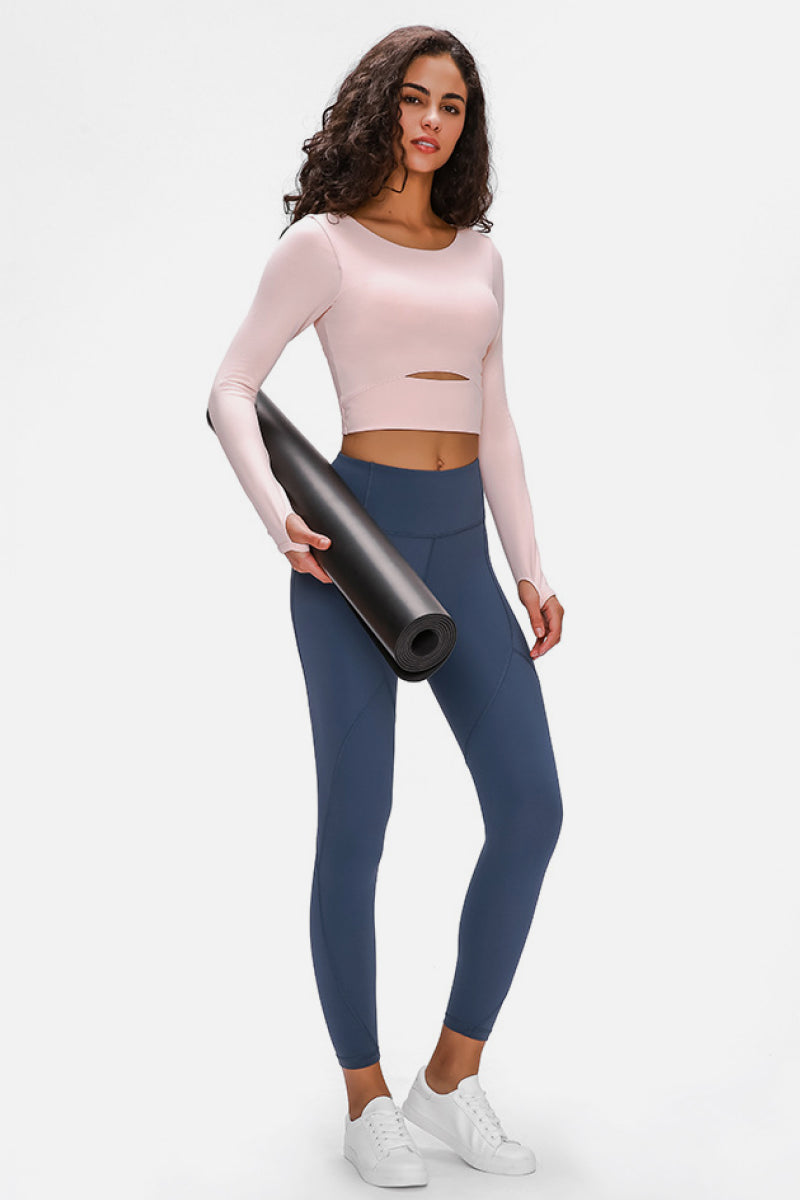 Woman wearing a long-sleeved, cropped workout top in pink, fitted with a support strap, for high-impact activewear.