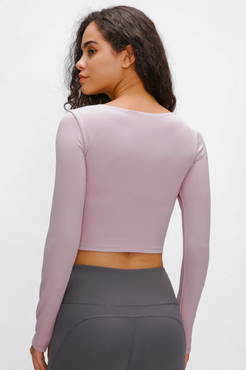 Woman wearing a long-sleeved, cropped workout top in lilac, fitted with a support strap, for high-impact activewear.