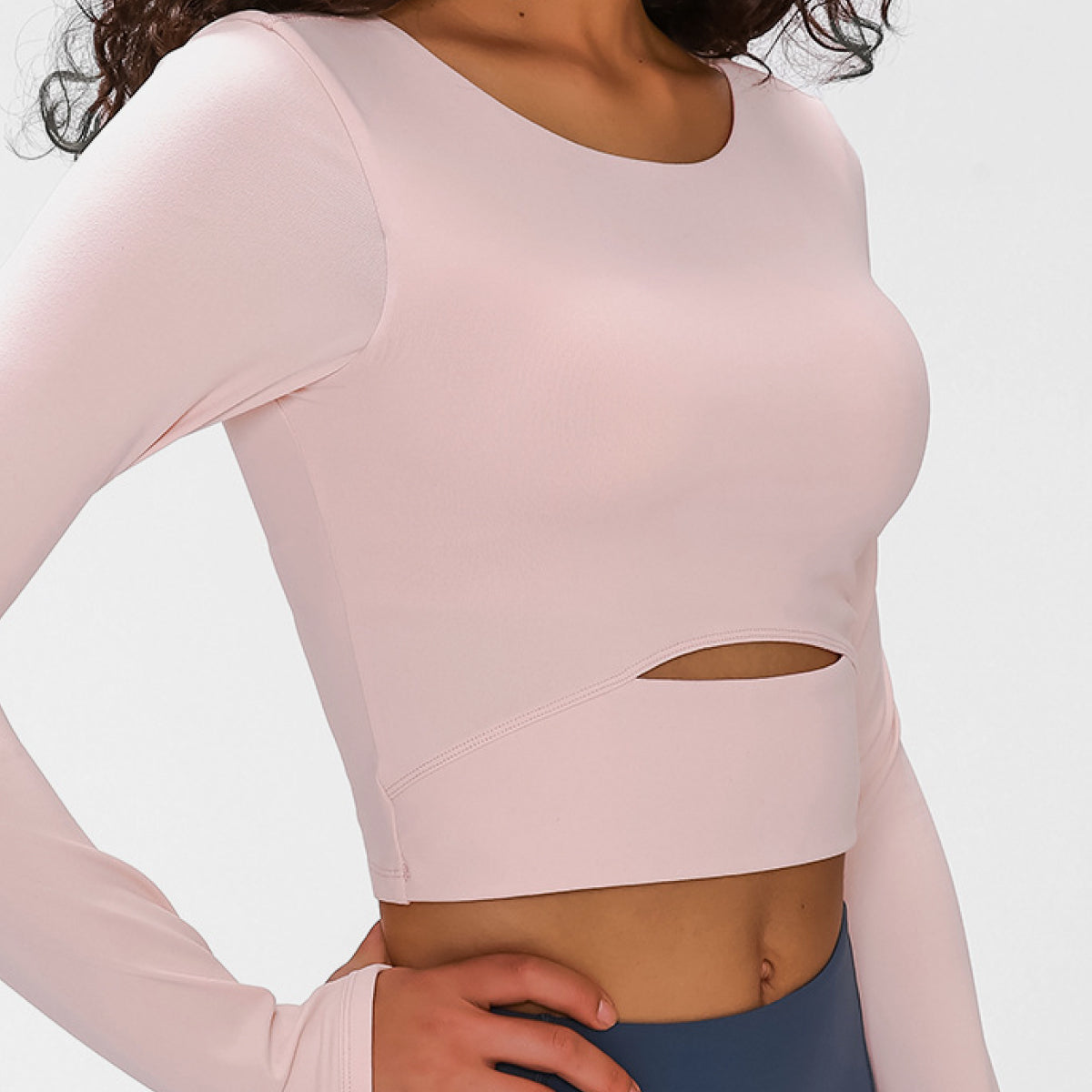 Woman wearing a long-sleeved, cropped workout top in pink, fitted with a support strap, for high-impact activewear.